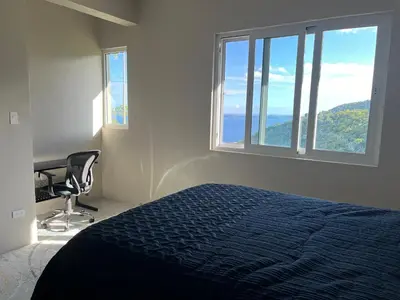 a bedroom with a bed and a desk and windows at Exquisitely Threadfall in Cane Garden Bay