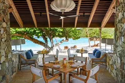 a dining room with a table and chairs and the ocean at Rosewood Little Dix Bay in Virgin Gorda Airport