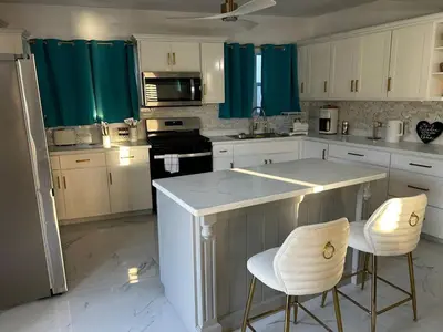 a kitchen with white cabinets and a counter with two chairs at Cane Garden Bay 2 bed Apt in Leonards