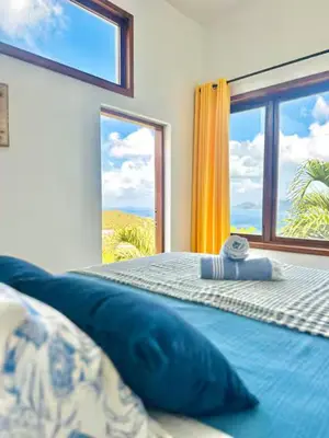 a bedroom with a blue bed with a large window at Solace Villa in Little Carrot Bay