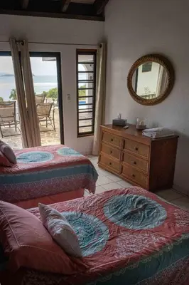 a bedroom with two beds and a dresser and a mirror at Villa ValMarc Mahoe Bay Virgin Gorda BVI in Virgin Gorda