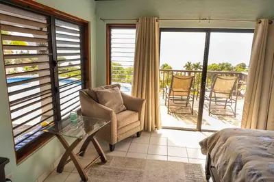 a bedroom with a bed and a balcony with chairs at Villa ValMarc Mahoe Bay Virgin Gorda BVI in Virgin Gorda