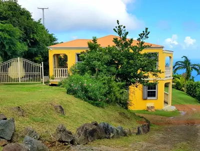 a yellow house on a hill with a yard at SUNFLOWER LANE QUEEN Balcony Room APARTMENT in Tortola Island