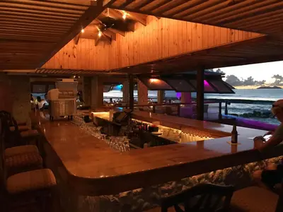 a bar in a restaurant with a view of the water at Sugar Mill Hotel in Great Carrot Bay
