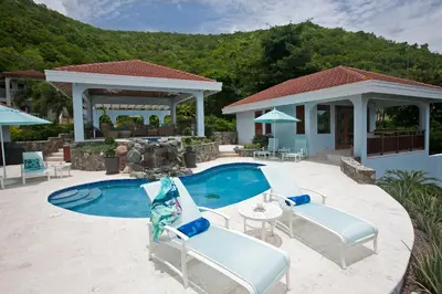 a swimming pool with two chairs and a house at BLUE LAGOON in Virgin Gorda