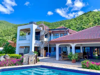 a villa with a swimming pool in front of a house at CARIBBEAN WIND in Virgin Gorda