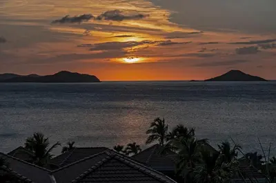 a sunset over the ocean with houses and palm trees at VILLA DEL SOLE in Virgin Gorda