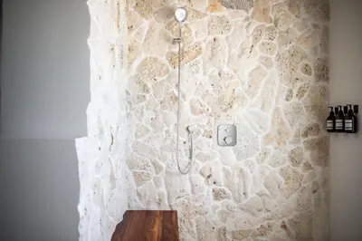 a bathroom with a stone wall with a shower at Long Bay Beach Resort in Tortola Island